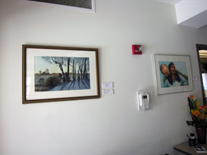 Photo of two paintings hanging on wall -- the closest one on the left features a landscape scene of a field with trees and shadows