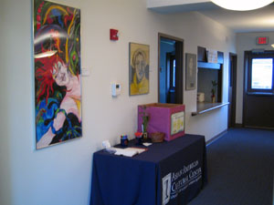 Photo of AACC space with artwork hanging on wall -- largest piece shows female figure with red hair against abstract colorful lines